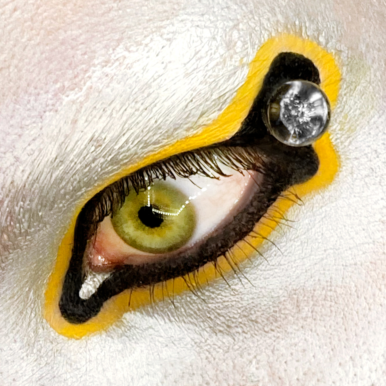 Macro shot of an eye with yellow and black graphic liner designs on silver skintone
